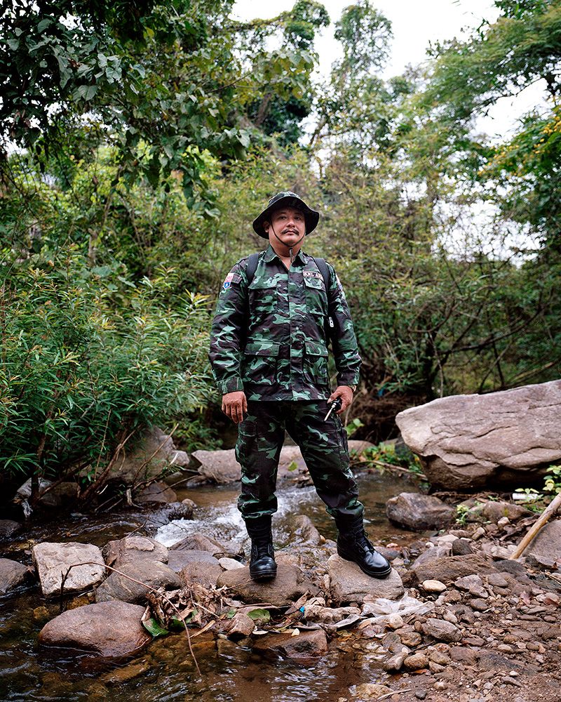 A Myanmar soldier stands on a pile of rocks in a creek holding a communication device.