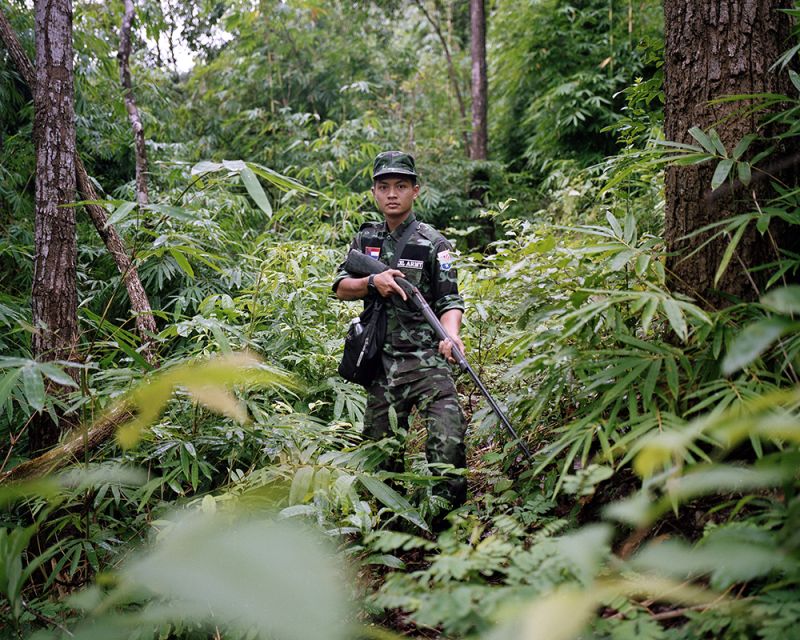 A young Myanmar holding a machine gun in a forest.