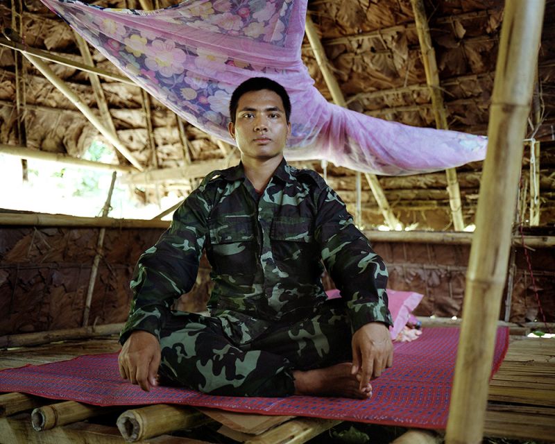 A young Myanmar soldier sitting in the lotus pose inside a hut. 
