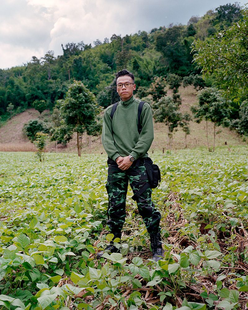 A young Myanmar soldier is posing for a portrait in the middle of a field.