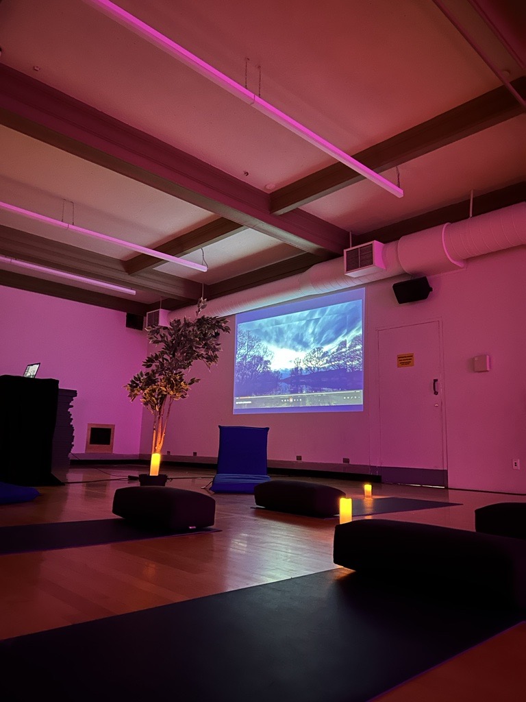 Dimly lit room with candles, plants, reclining chairs and mats. Soothing nature videos are projected onto the wall.