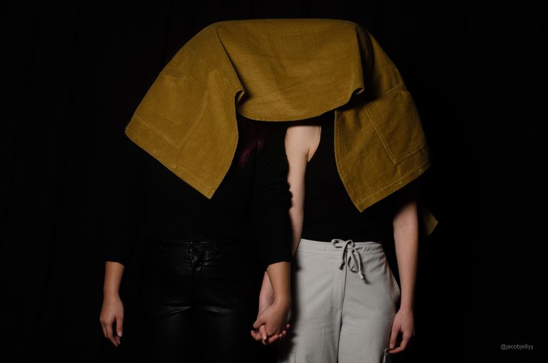 Two models standing and holding hands with their heads covered by towel.