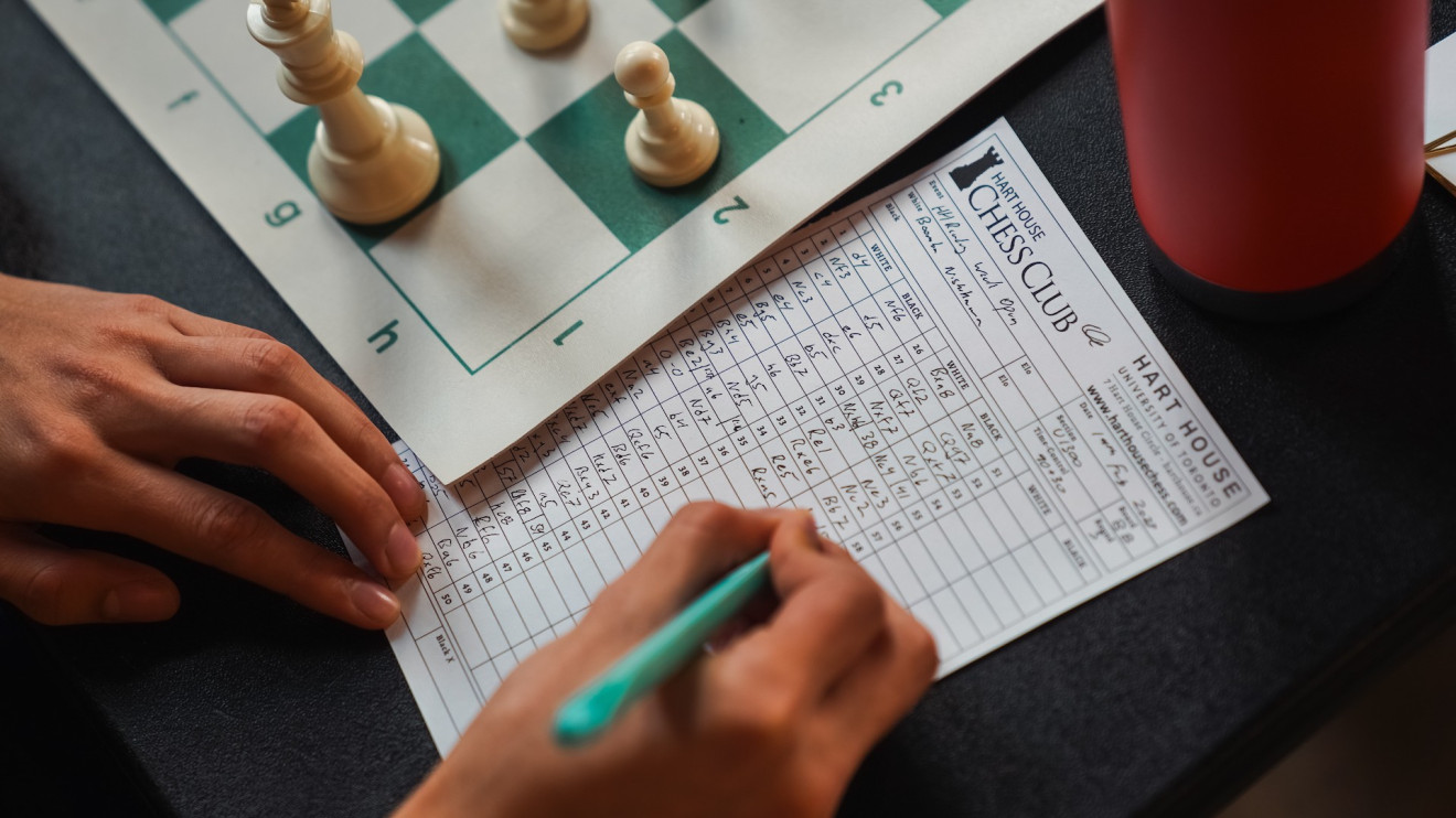 Image of a chess player notating moves next to a chessboard.