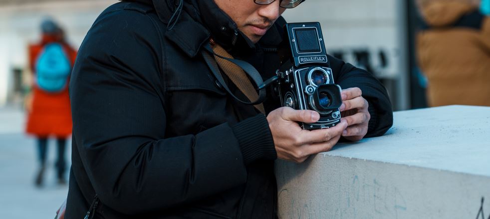 A man is positioning his analog camera for outdoor urban photography. 