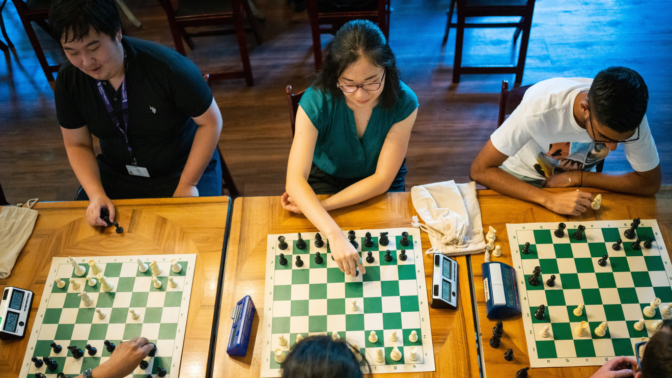A top-down photograph of three pairs of chess players, each in the middle of a blitz game against  their opponent.