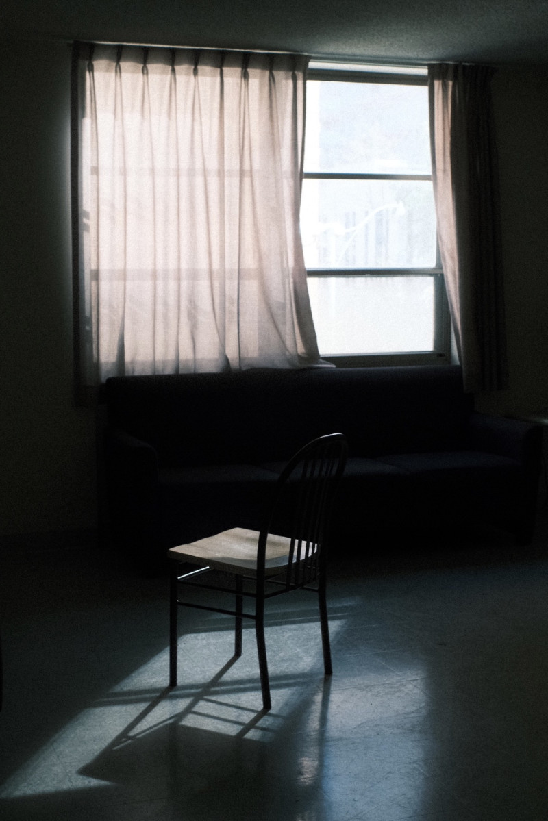 A dramatic view of a chair in an empty room in front of a large window with curtains. 