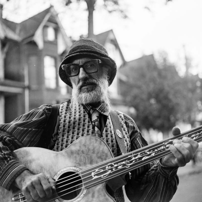 A portrait of a musician playing the guitar in a residential neighbourhood. 