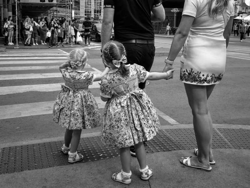 Two adults and two children in floral dresses waiting to cross an intersection. 