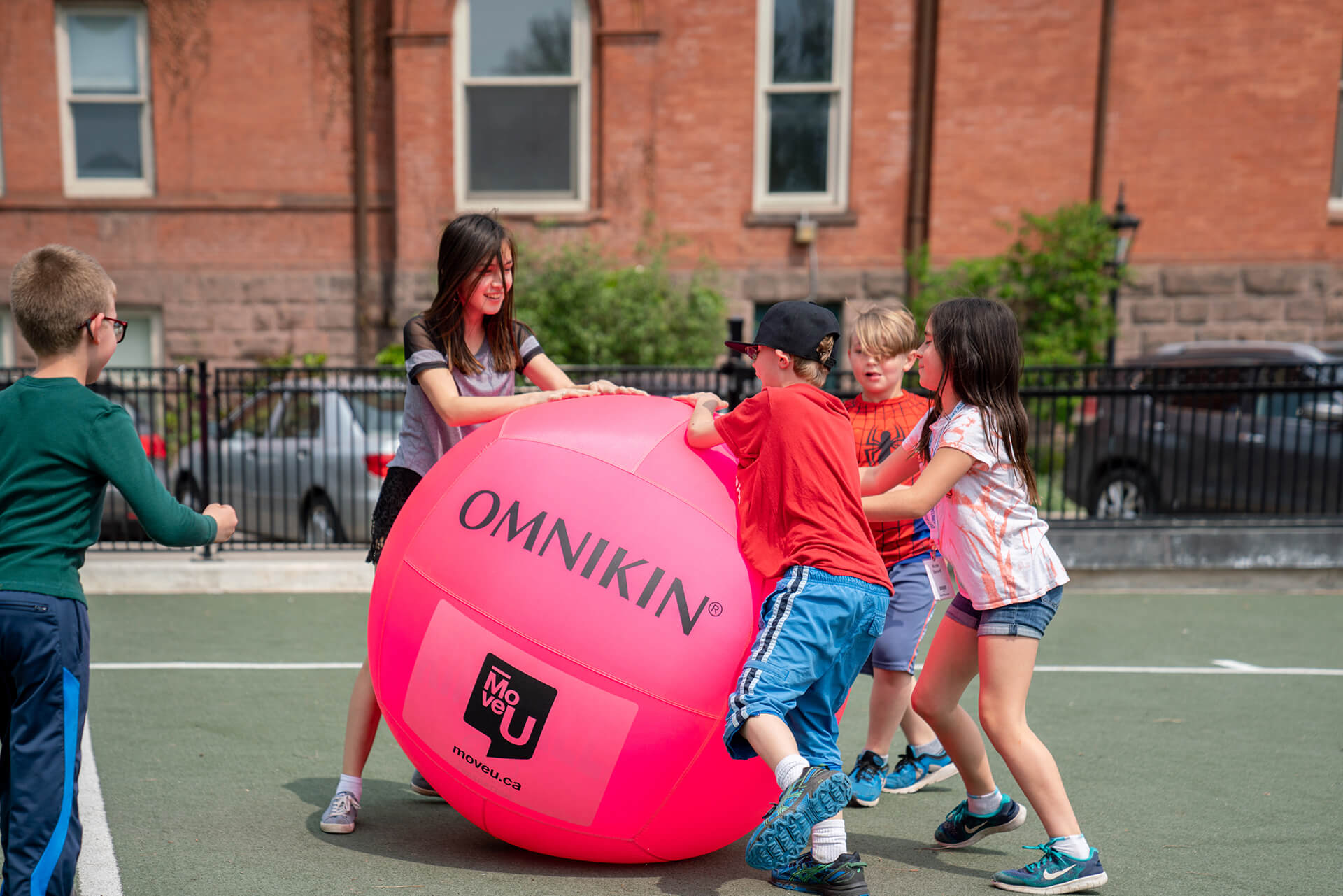 3 kids rolling an extra large playing ball on a large play court