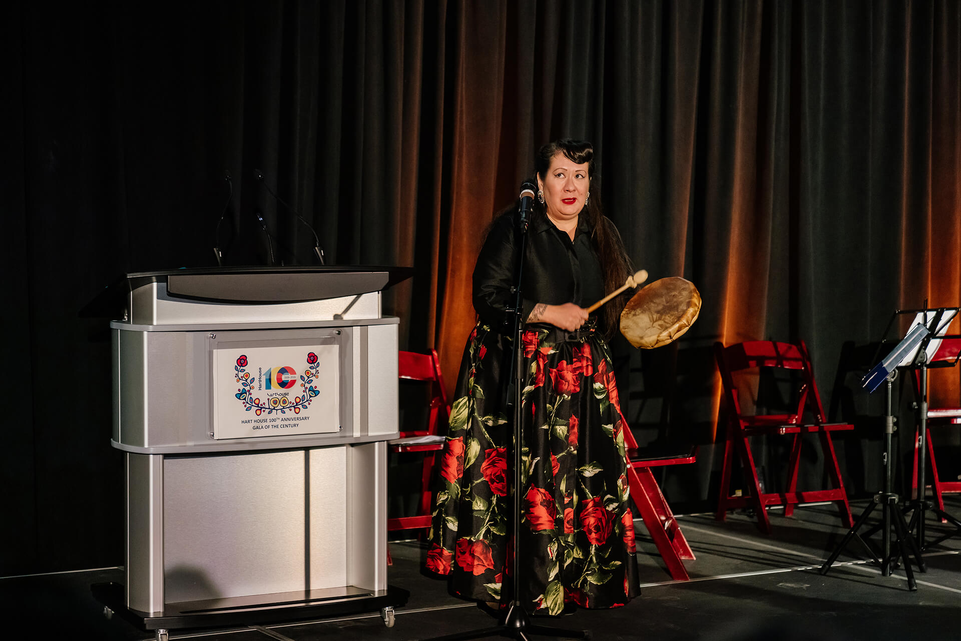 A woman is playing a frame drum and sing on stage 