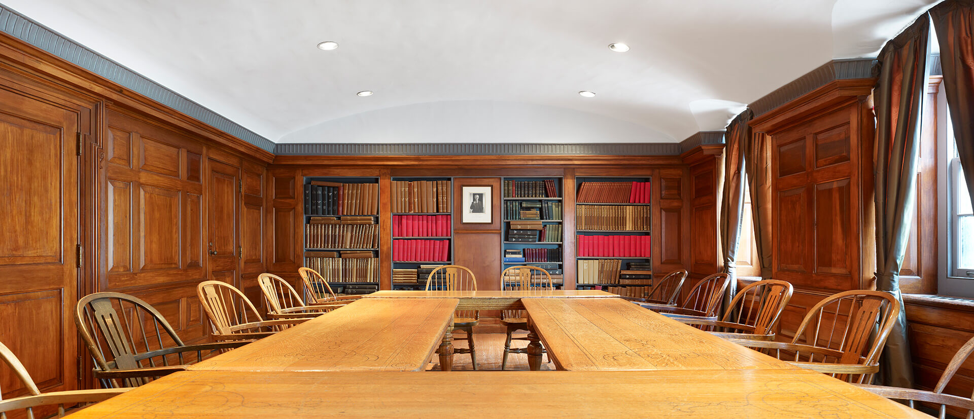 A large meeting table set in a room with oak paneling, bookcases, a fireplace, and period tables and chairs.