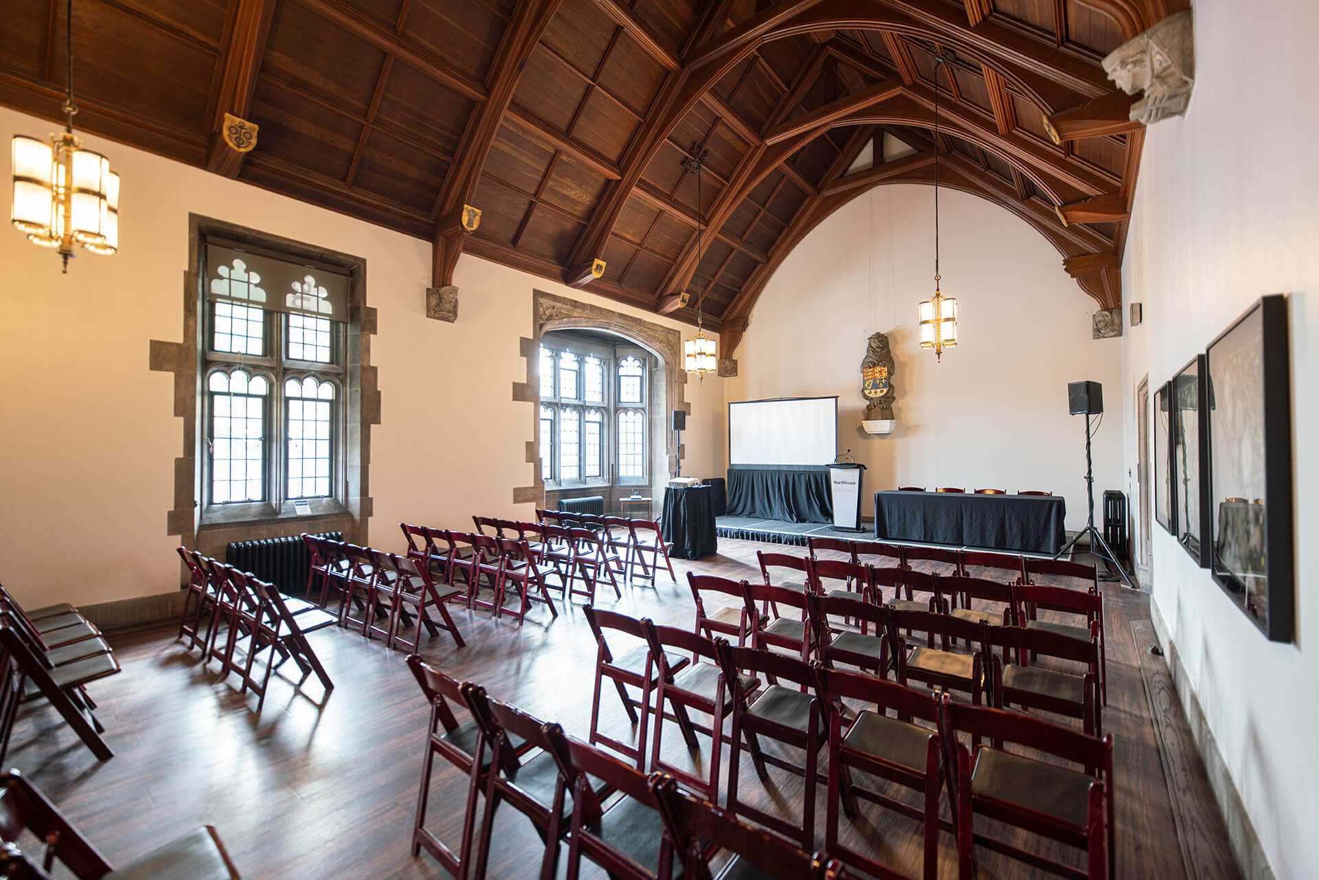 A large room with hardwood floors, gothic windows, vaulted wooden ceiling and seating arranged for an event