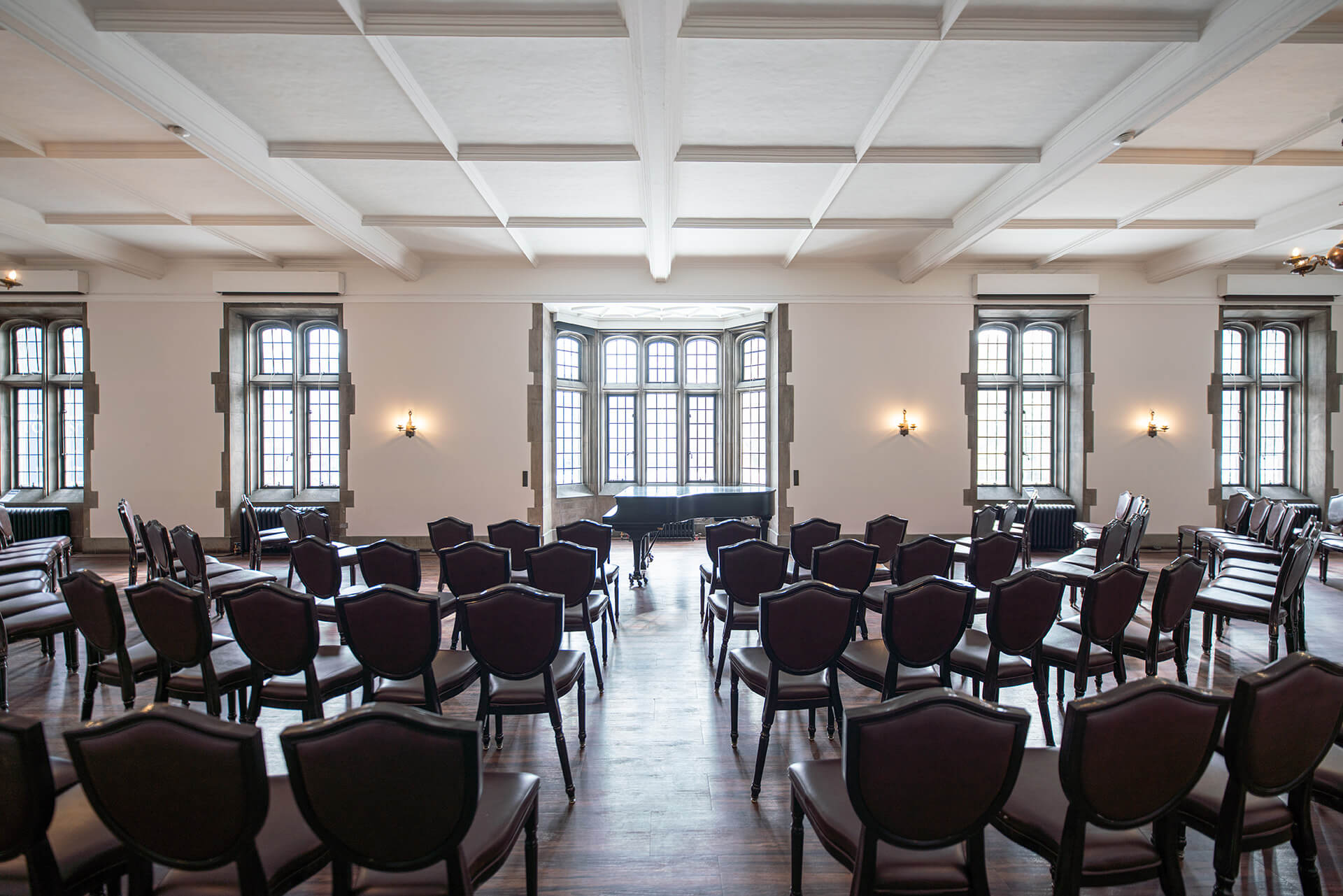 A large room with hardwood floors, gothic windows and seating arranged for an event