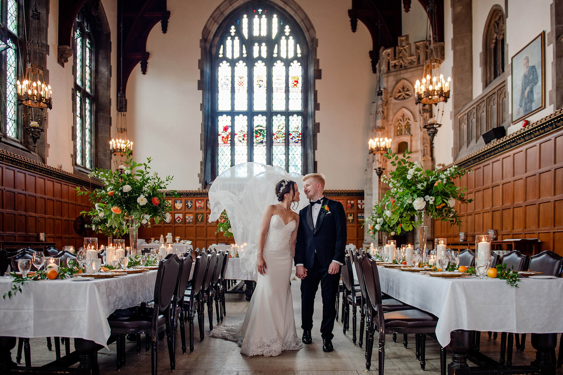A happy couple stands in the Great Hall, surrounded by tables awaiting their dinner guests