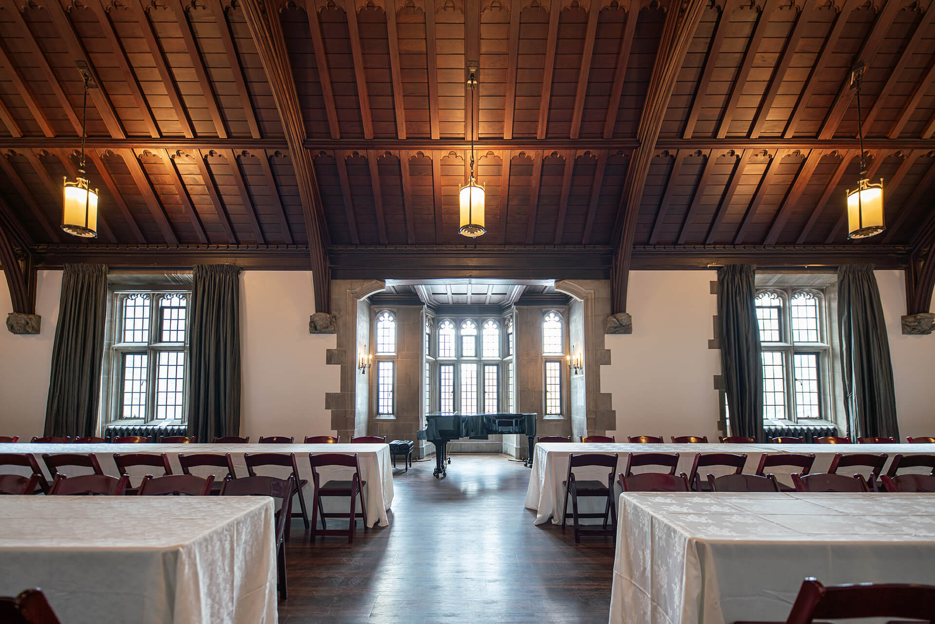 A large room with hardwood floors, gothic windows, vaulted wooden ceiling and tables with seating arranged for an event