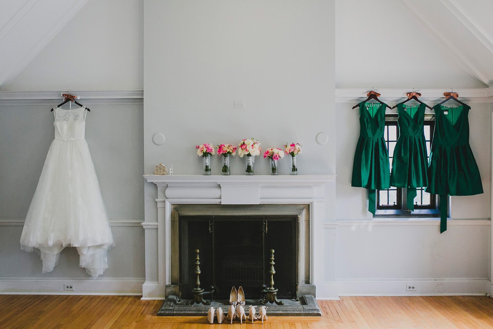 A bridal gown and bridesmaid dresses hang in a bright room with a fireplace