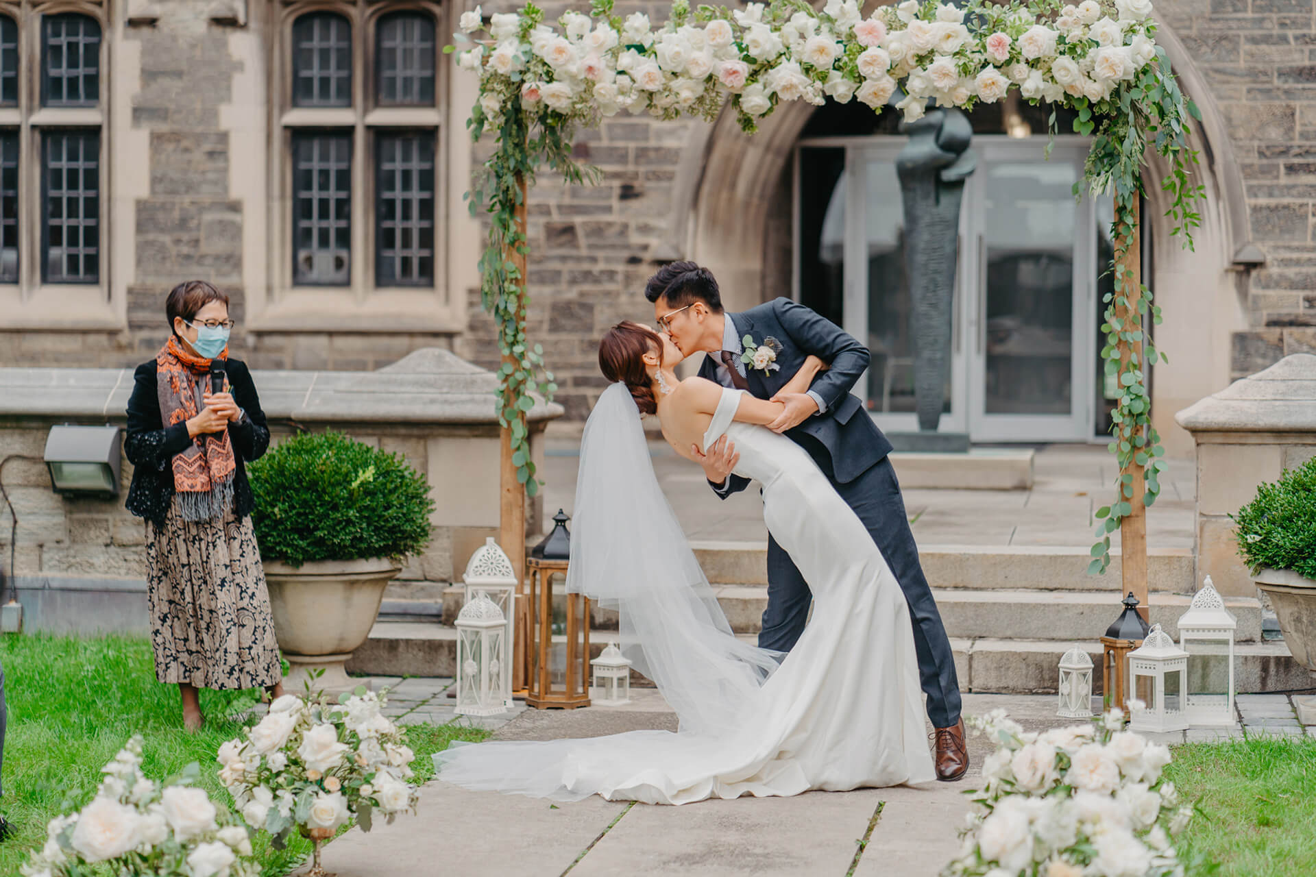 A couple has their first kiss after their vows, surrounded by flowers